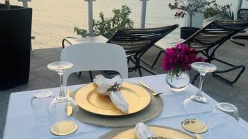 A table set for a meal with gold plates, white napkins, and wine glasses, overlooking a body of water.