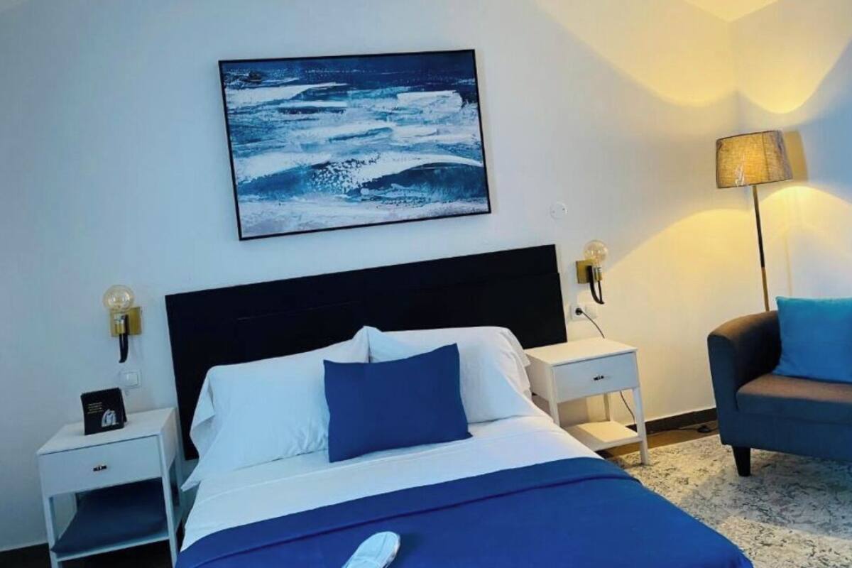 Une chambre d’hôtel comprenant un lit, une table de chevet, une chaise, une lampe et une œuvre d’art accrochée au mur.