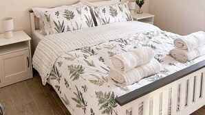 Ein ordentlich bezogenes Bett mit Blumenmuster, eine Nachttischlampe und eine kleine Pflanze auf dem Nachttisch.