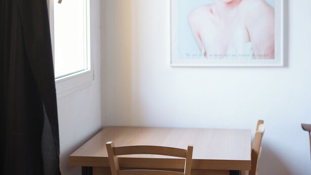 Un comedor con una mesa y sillas de madera, un cuadro en la pared y una ventana con cortina.