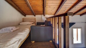 Una habitación pequeña y acogedora con techo de madera y una cama litera. Hay un sofá pequeño y una ventana que deja entrar luz natural.