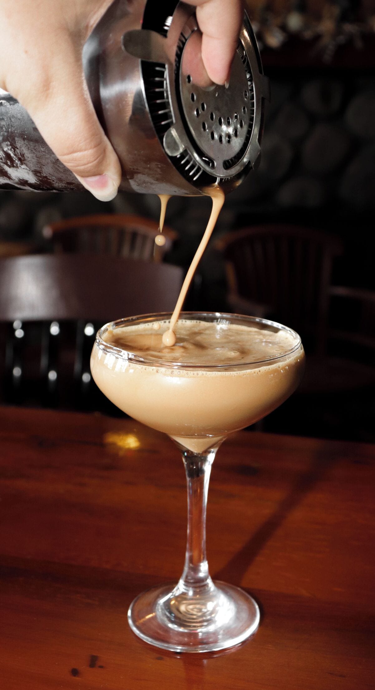 A hand pouring a beverage into a martini glass.