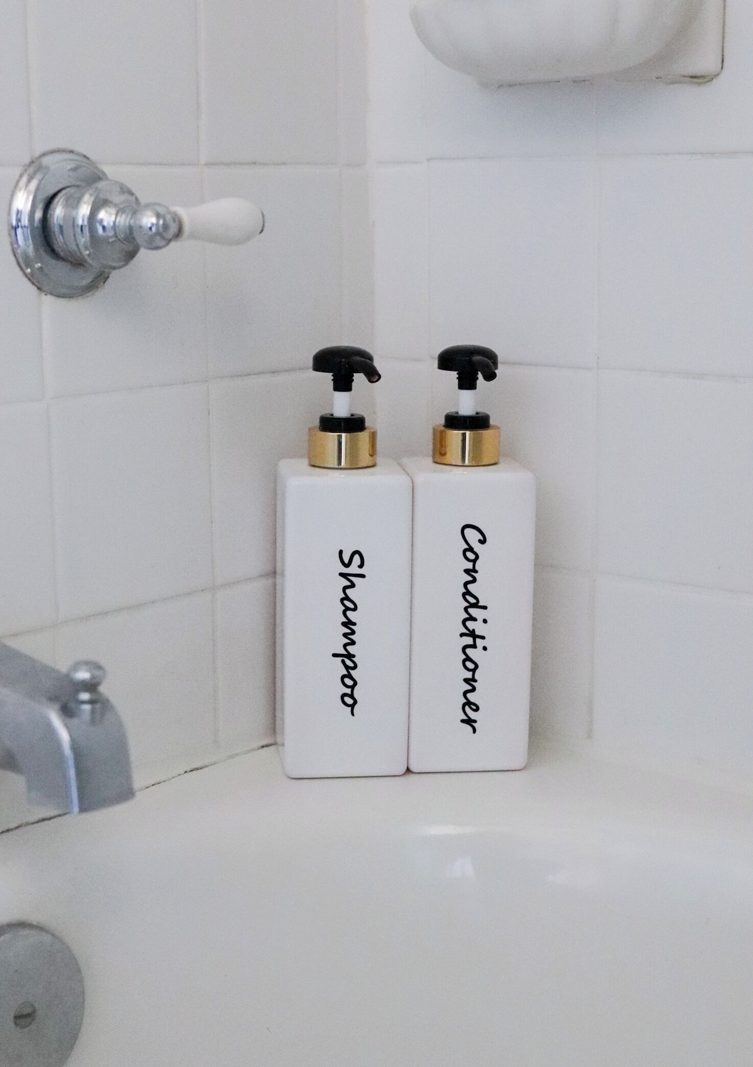 Two white bottles with black pumps labeled 'Shampoo' and 'Conditioner' on a bathroom counter.