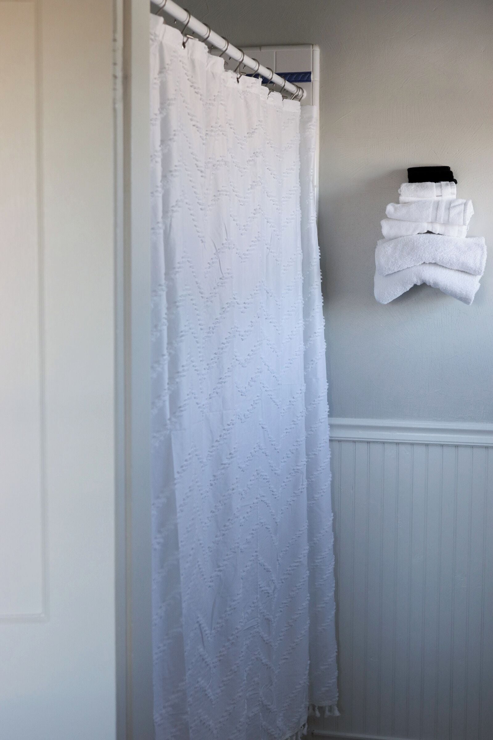 A bathroom with a white shower curtain, a stack of white towels on a wall, and a white radiator.