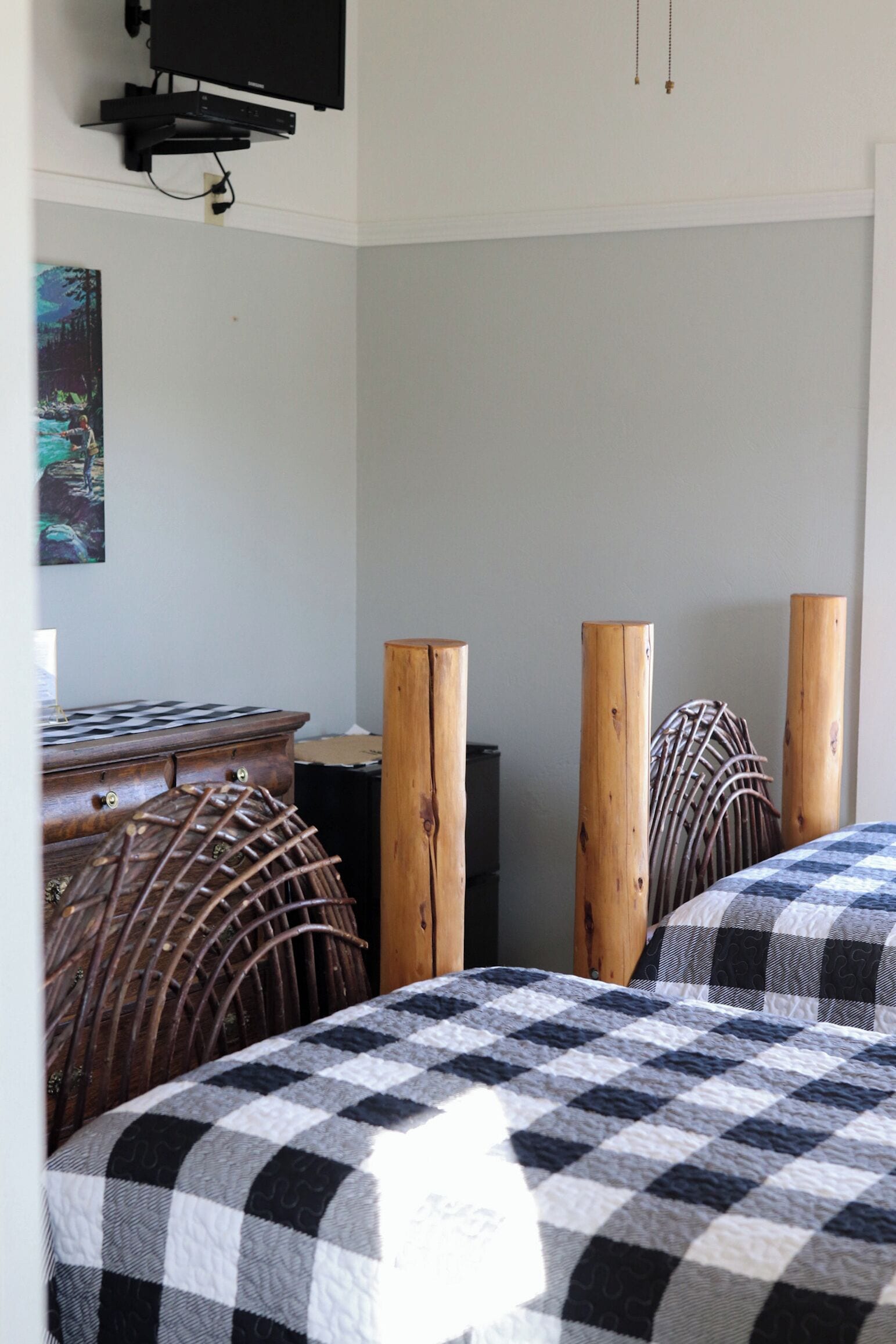 A bedroom with two beds, a dresser, and a television mounted on the wall.