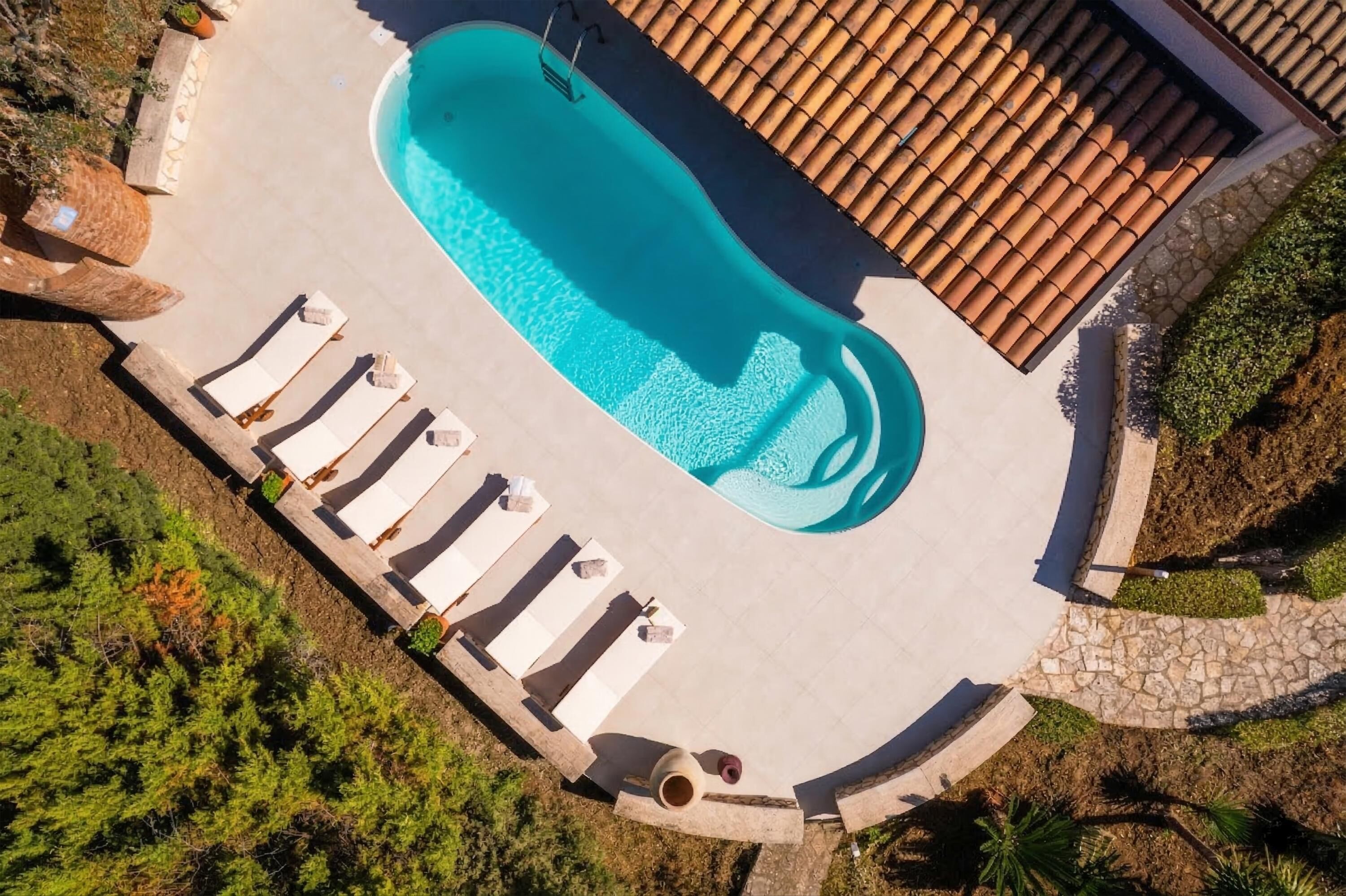 Vue aérienne d’une piscine avec des chaises longues et un toit recouvert de tuiles.