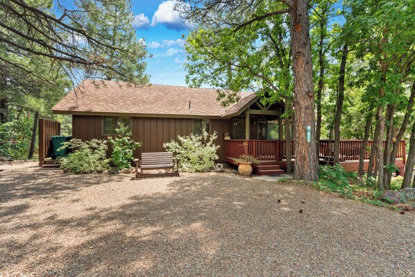 A cabin with a gravel driveway, wooden deck, and a bench.