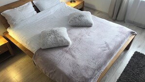 A neatly made bed with white linens and two fluffy pillows, a wooden headboard, a bedside table with a lamp, and a dark rug on the floor. - Modern Apartment (Brasov)