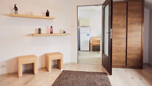 A room with a wooden wardrobe, two small stools, and shelves with decorative items. - Modern Apartment (Brasov)