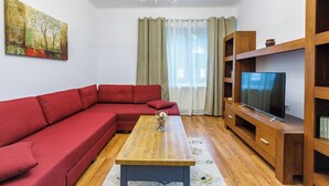 A living room with a red sofa, wooden coffee table, and a TV on a wooden stand. - Modern Apartment (Brasov)