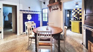 A dining area with a round wooden table and white chairs, a blue tiled wall, and a hanging light fixture. - La Maisonette Cambon, Charme en Camargue (Saintes-Maries-de-la-Mer)