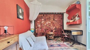 A cozy living room with a red wall, a patterned tapestry, a wooden sofa, a globe, and a red shelf with decorative items. - La Maisonette Cambon, Charme en Camargue (Saintes-Maries-de-la-Mer)
