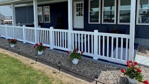 Een huis met een overdekte veranda, een witte balustrade en potplanten.