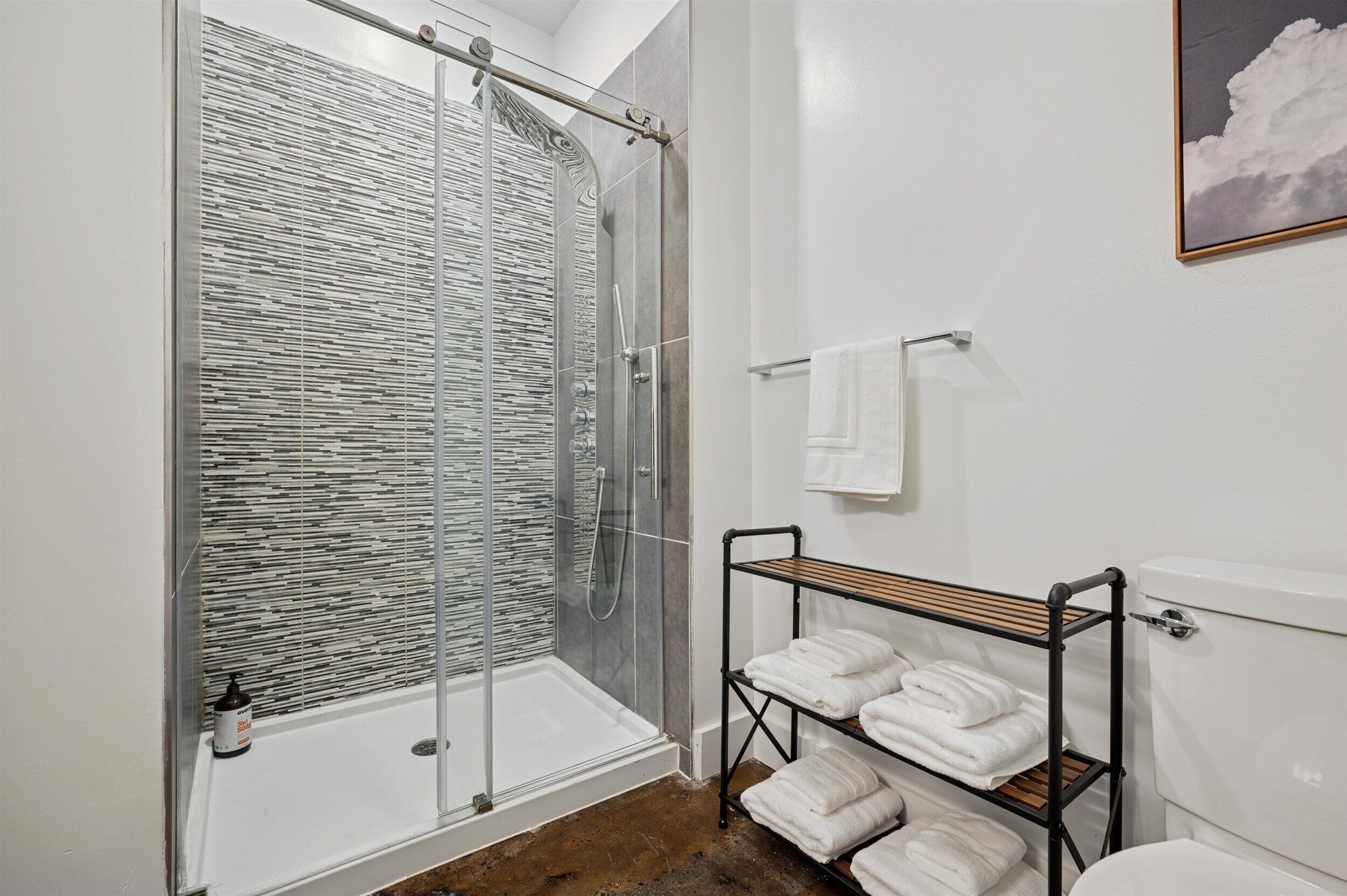 A modern bathroom with a glass shower enclosure, a white toilet, and a towel rack with neatly folded towels.