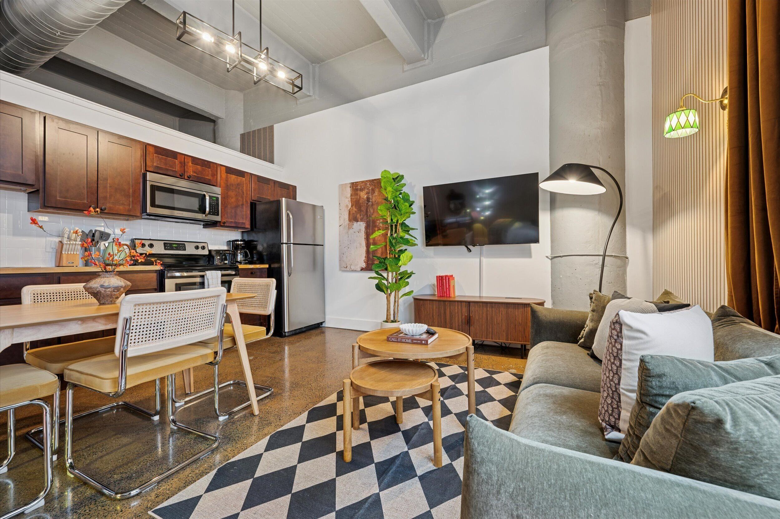 A modern kitchen with stainless steel appliances, a dining area with a checkered rug, and a living room with a sofa and a coffee table.