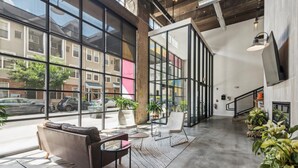 A spacious lobby with large windows, a modern sofa, a small table, and potted plants. - Storehouse Lofts (Philadelphia)