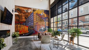 A spacious lobby with a large mural of a cityscape, modern furniture, and large windows offering a view of the street. - Storehouse Lofts (Philadelphia)