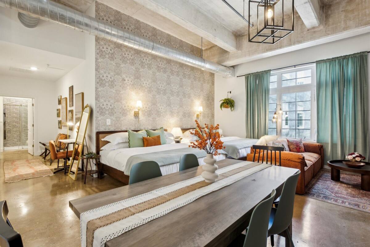 A modern hotel room with a large bed, a dining table, and a seating area.