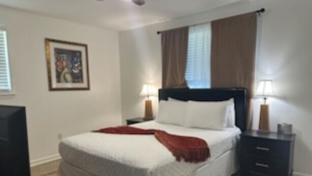 Een slaapkamer met een bed, nachtkastjes, een lamp en een schilderij aan de muur.