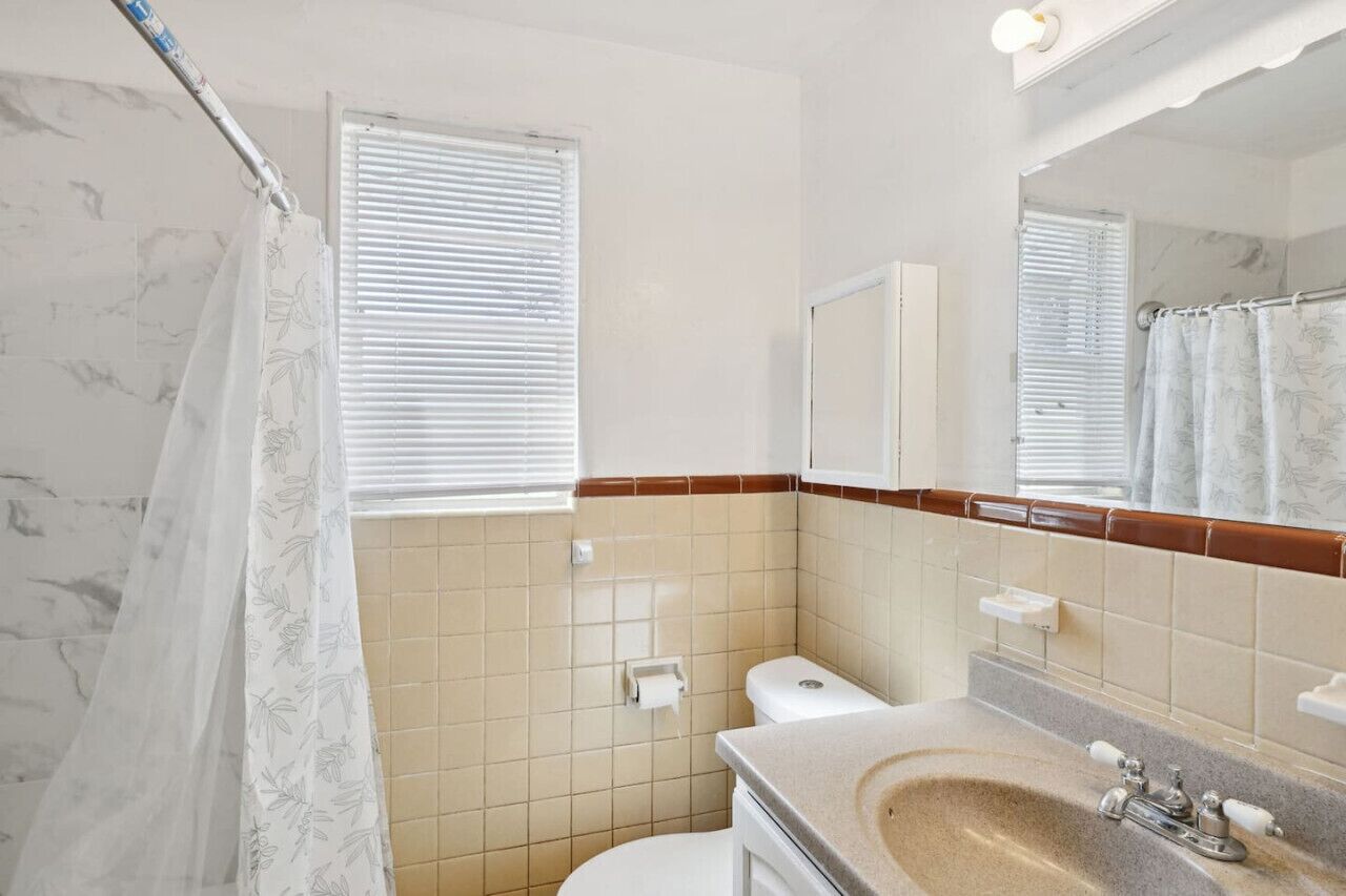 Ein Badezimmer mit Toilette, Waschbecken, Spiegel und Duschvorhang.