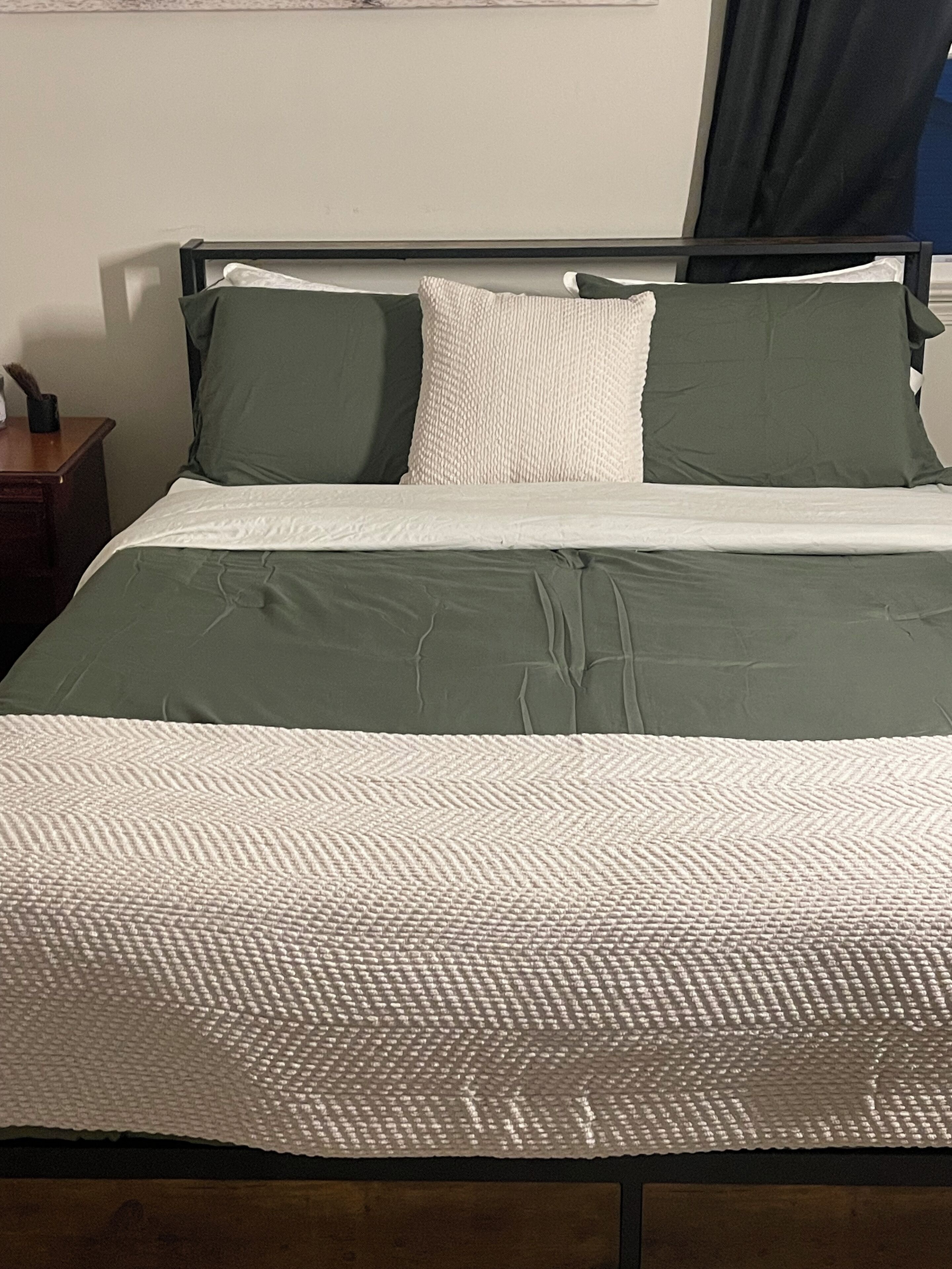 A bed with a green and white bedspread, two pillows, and a wooden headboard.