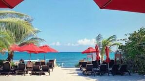 Un área de piscina frente a la playa, con sombrillas rojas y sillas reclinables.