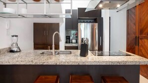 Una cocina moderna con encimeras de granito, electrodomésticos de acero inoxidable y taburetes de bar de madera.