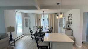 Cozinha moderna com ilha central, área de jantar com cadeiras, lustre e relógio na parede.