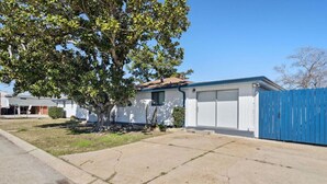Ein eingeschossiges Haus mit Garage, einem blauen Zaun und einem Baum im Vorgarten.