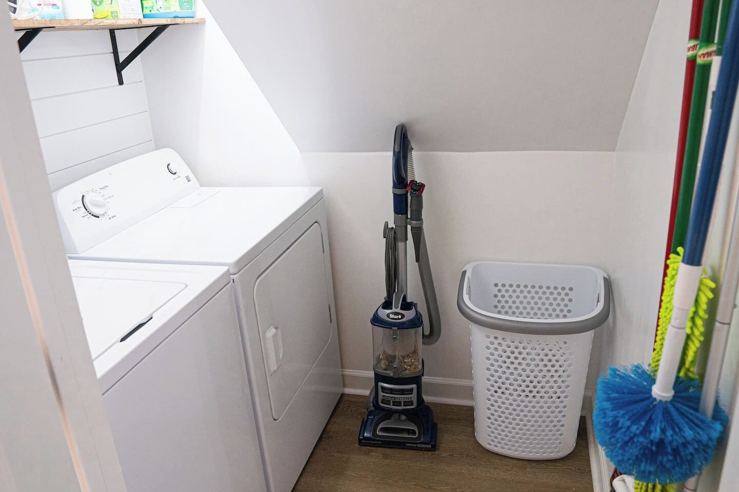 Un espace dédié à la lessive, comprenant un lave-linge, un aspirateur et un panier à linge.
