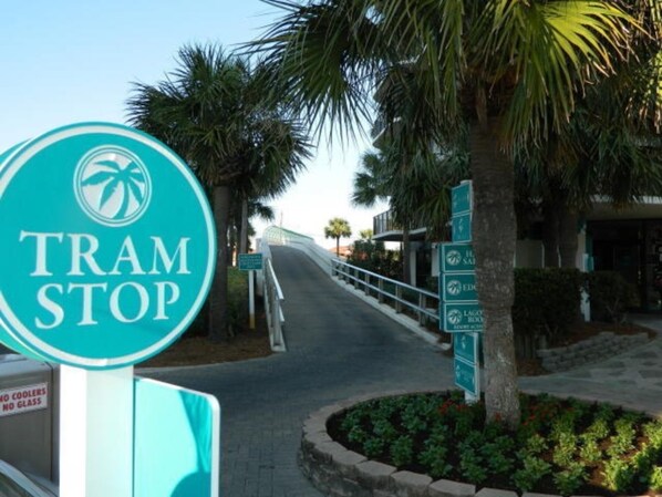 A tram stop sign with palm trees and a pathway leading to a building. - Seabreeze Bliss @ Edgewater - 5th floor, private balcony, direct beachfront (Panama City Beach)