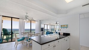 A spacious kitchen with a central island, large windows with ocean views, and a dining area with chairs and a table. - Seabreeze Bliss @ Edgewater - 5th floor, private balcony, direct beachfront (Panama City Beach)