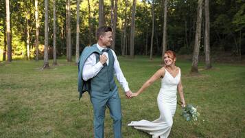 A couple holding hands in a grassy outdoor area with trees in the background.