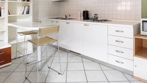 A modern kitchen with white cabinets, a built-in bookshelf, a dining area with a chair, and a tiled floor. - Studio Calari alle Mura by Wonderful Italy (Bologna)