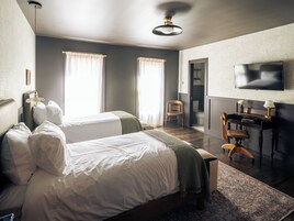 Hotelkamer met twee bedden, een bureau, een stoel, een televisie en een badkamer die door een open deur zichtbaar is.