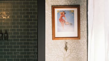 A bathroom with a patterned wallpaper, a framed picture on the wall, and a tiled shower area.