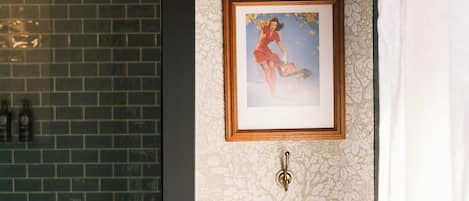 Een badkamer met behang met een patroon, een inlijsting foto aan de muur en een betegelde douchehoek.