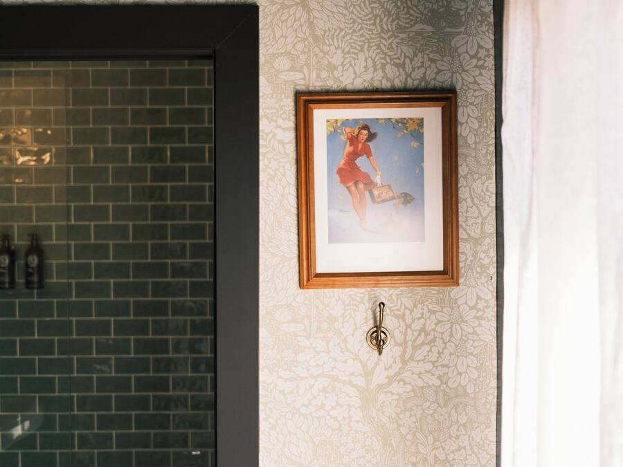 A bathroom with a patterned wallpaper, a framed picture on the wall, and a tiled shower area.