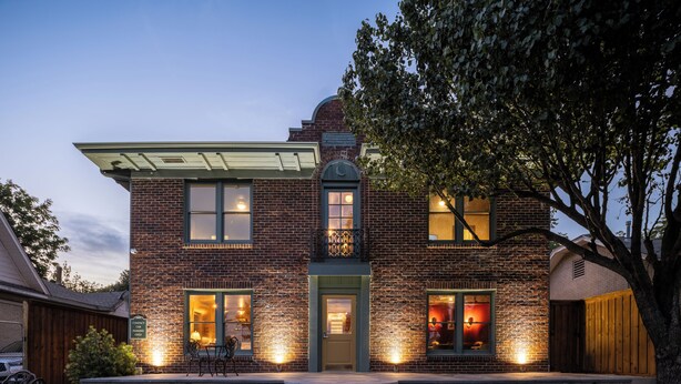 A two-story brick house with a front porch, a small garden, and a patio with outdoor furniture.