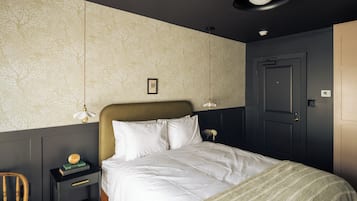 A bedroom with a bed, a nightstand, a chair, a door, and a wall with a floral pattern.