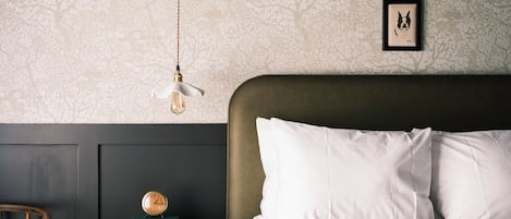 Una cama bien hecha con sábanas blancas, cabecera oscura y un cuadro en la pared.