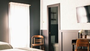 A bedroom with a bed, two chairs, a desk, a television, and a bathroom visible through an open door.