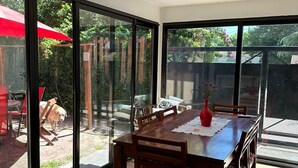 A dining area with a large table and chairs, a red umbrella, and a view of a backyard with a wooden fence and greenery. - Anas inn (Ezeiza)
