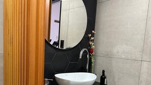 A modern bathroom with a round mirror, a white sink, and a wooden cabinet.