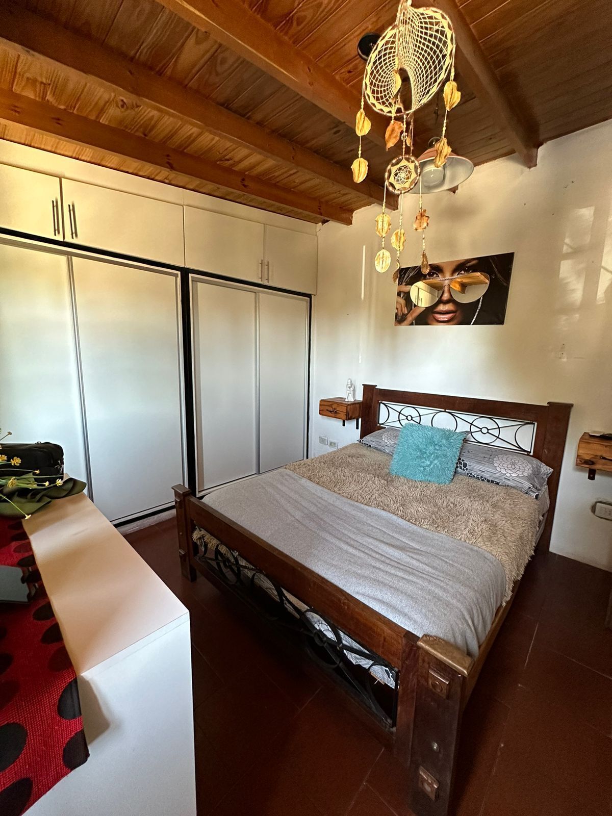 A bedroom with a wooden bed, a white wardrobe, and a ceiling with wooden beams.