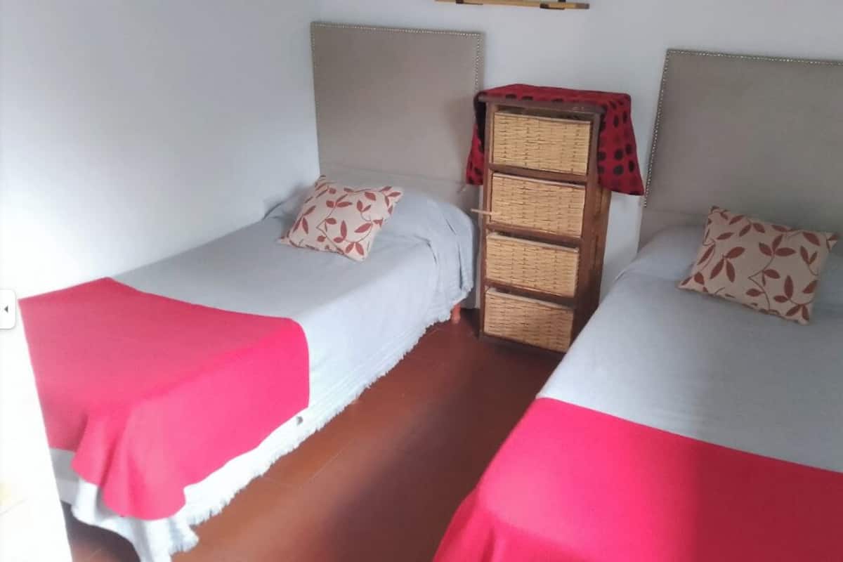 Two single beds with red and white bedding, a wooden chest of drawers, and a small shelf above the beds.