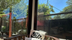 A wooden chair with cushions in a room with a large window overlooking a fenced outdoor area.