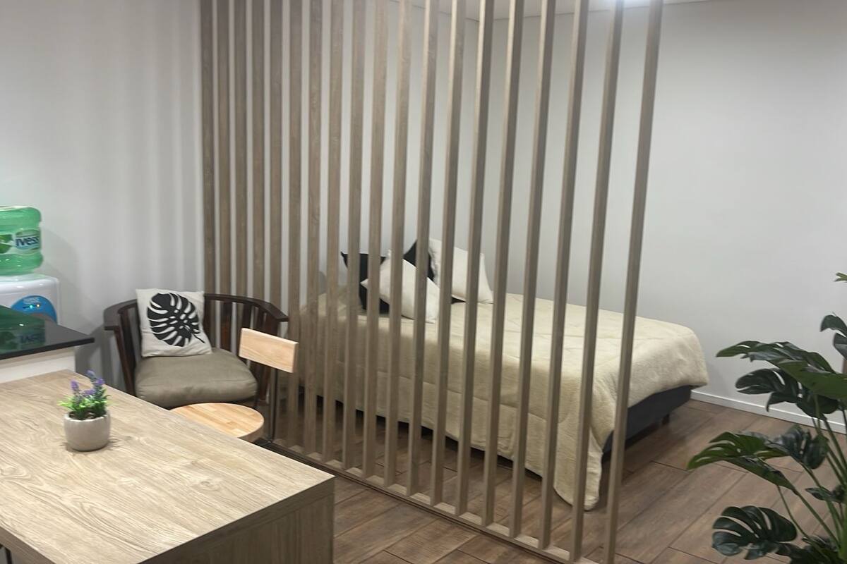 A modern room with a bed, a dining table with chairs, a small potted plant, and a water dispenser.
