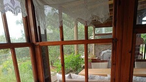 A cozy room with a wooden bench, a table with a vase of flowers, and a view of greenery outside. - Dilara Huzur Motel (Ayvacik)