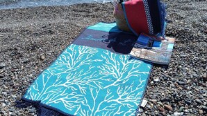 A beach with a blue patterned mat and a red bag on the pebbles. - Dilara Huzur Motel (Ayvacik)